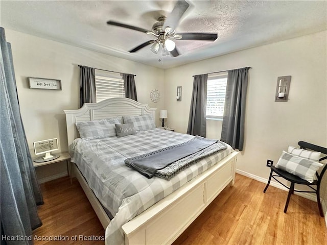 bedroom featuring ceiling fan, a textured ceiling, light wood-style flooring, and baseboards