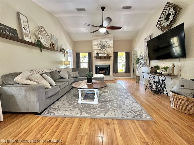 living area with visible vents, a ceiling fan, a large fireplace, wood finished floors, and baseboards