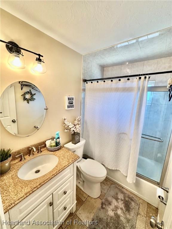 full bath with shower / bath combination with curtain, vanity, toilet, and a textured ceiling