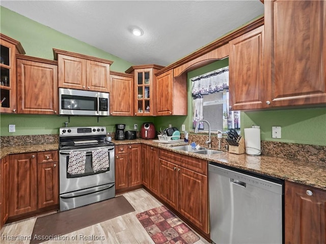 kitchen featuring appliances with stainless steel finishes, light wood-type flooring, stone countertops, vaulted ceiling, and sink