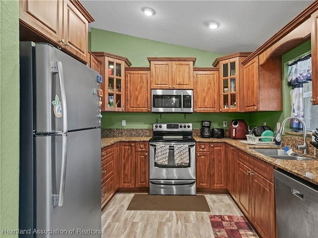 kitchen featuring vaulted ceiling, light hardwood / wood-style floors, sink, light stone countertops, and appliances with stainless steel finishes