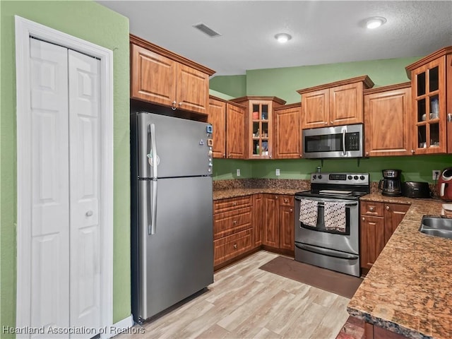 kitchen featuring light hardwood / wood-style floors, stainless steel appliances, vaulted ceiling, stone counters, and sink