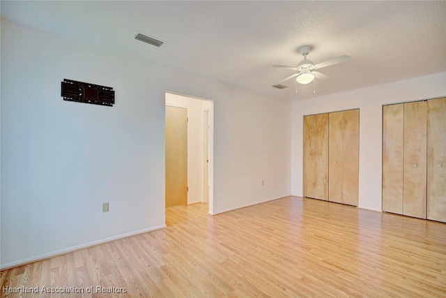 unfurnished bedroom featuring a textured ceiling, two closets, light hardwood / wood-style flooring, and ceiling fan