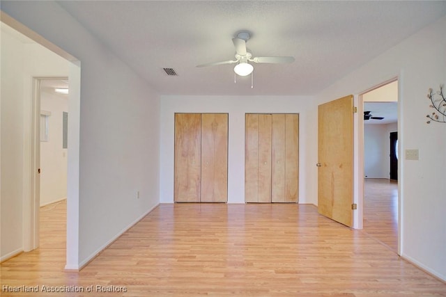 unfurnished bedroom with ceiling fan, light hardwood / wood-style flooring, and two closets