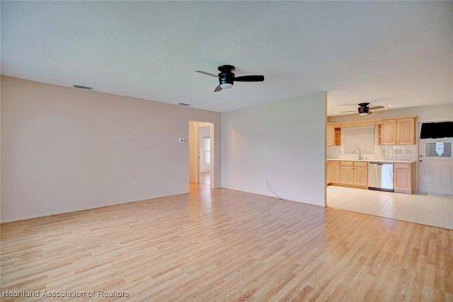 unfurnished living room featuring ceiling fan, sink, a textured ceiling, and light wood-type flooring