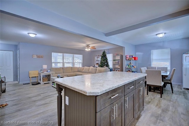 kitchen featuring fridge, a center island, ceiling fan, light hardwood / wood-style floors, and beam ceiling