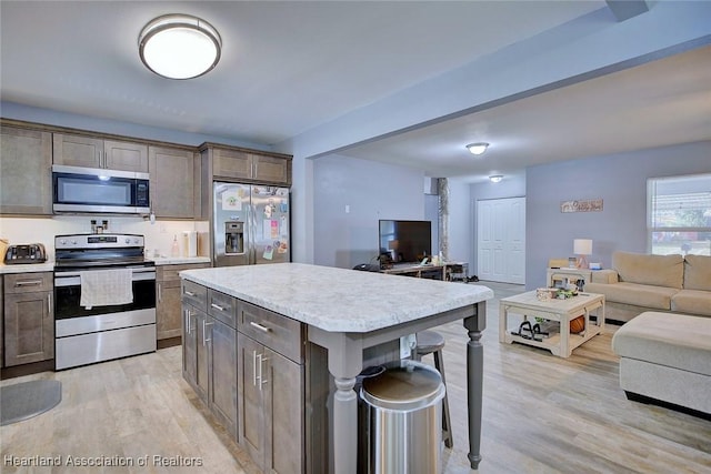 kitchen with light hardwood / wood-style flooring, a kitchen island, a kitchen breakfast bar, and appliances with stainless steel finishes