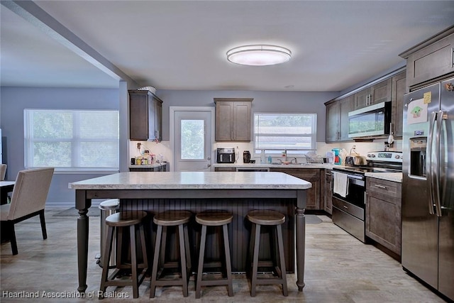 kitchen featuring sink, appliances with stainless steel finishes, a kitchen island, light hardwood / wood-style floors, and a kitchen bar