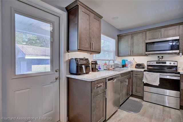 kitchen featuring dark brown cabinetry, stainless steel appliances, sink, and light hardwood / wood-style flooring