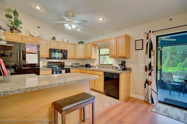 kitchen with light stone countertops, a kitchen breakfast bar, light brown cabinetry, black appliances, and light wood-type flooring