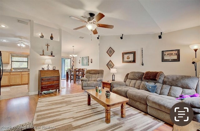 living room with ceiling fan with notable chandelier, light hardwood / wood-style flooring, lofted ceiling, and sink