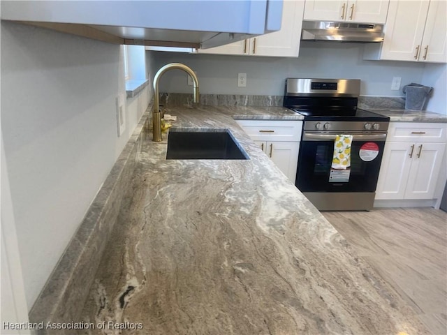 kitchen with white cabinetry, sink, light stone counters, and stainless steel range oven