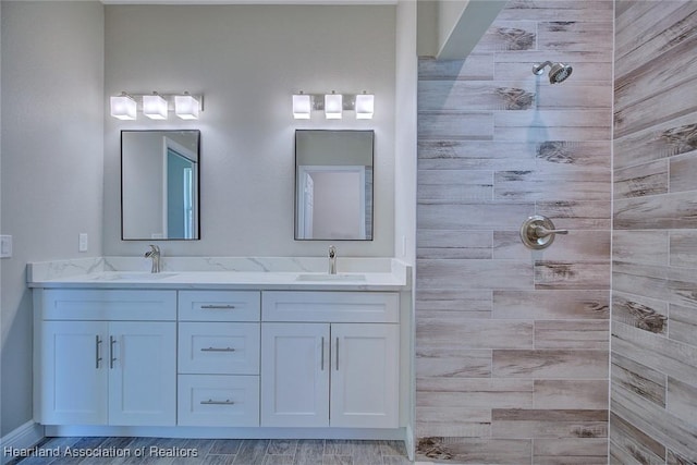 bathroom with a sink, baseboards, double vanity, and tiled shower