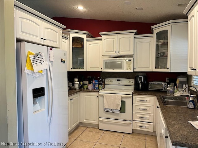 kitchen with sink, white cabinetry, a textured ceiling, white appliances, and light tile patterned flooring