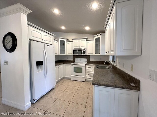 kitchen featuring white appliances, a sink, white cabinetry, dark countertops, and glass insert cabinets