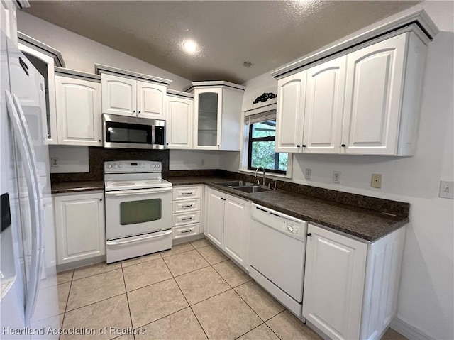 kitchen featuring white appliances, dark countertops, glass insert cabinets, white cabinetry, and a sink