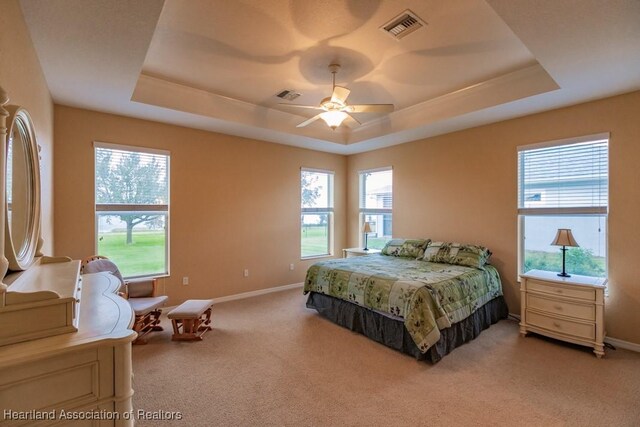 bedroom featuring ceiling fan, a raised ceiling, light carpet, and multiple windows