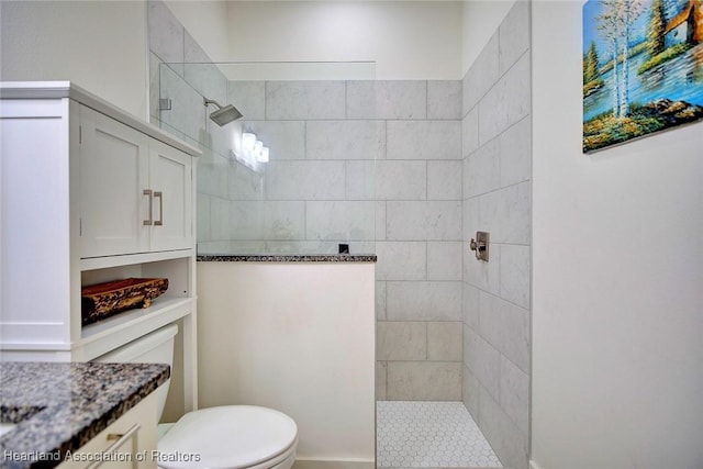 bathroom with toilet, a tile shower, and vanity