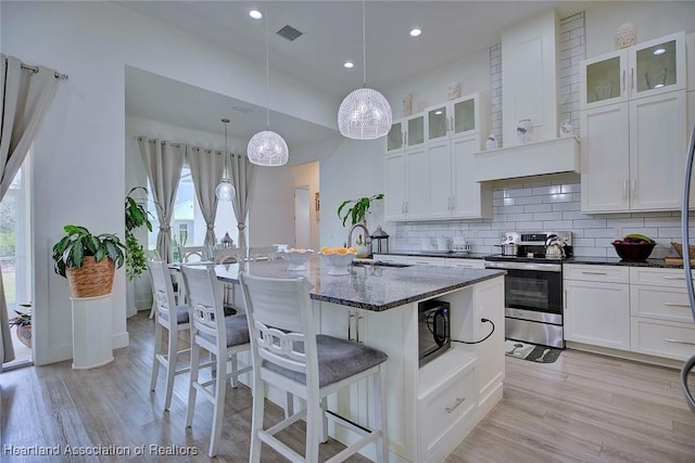 kitchen featuring dark stone countertops, stainless steel electric range, a breakfast bar, hanging light fixtures, and white cabinets