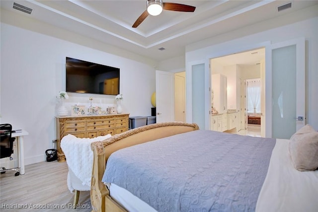 bedroom with ceiling fan, ensuite bath, light wood-type flooring, and a tray ceiling