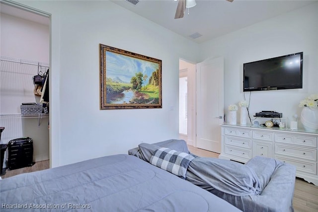 bedroom featuring ceiling fan, a closet, a walk in closet, and light wood-type flooring