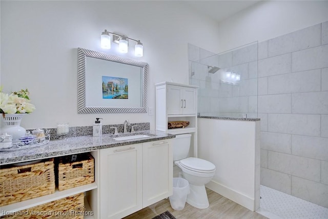 bathroom featuring hardwood / wood-style flooring, tiled shower, vanity, and toilet