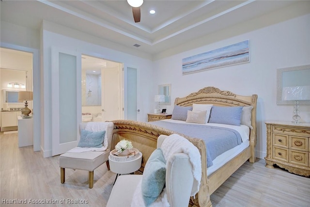 bedroom with ceiling fan, light hardwood / wood-style floors, a raised ceiling, and ensuite bath