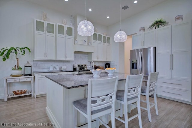 kitchen featuring stainless steel refrigerator with ice dispenser, an island with sink, dark stone countertops, and white cabinetry