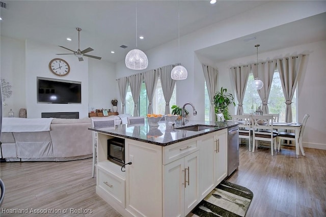 kitchen with pendant lighting, white cabinetry, dark stone counters, sink, and a kitchen island with sink