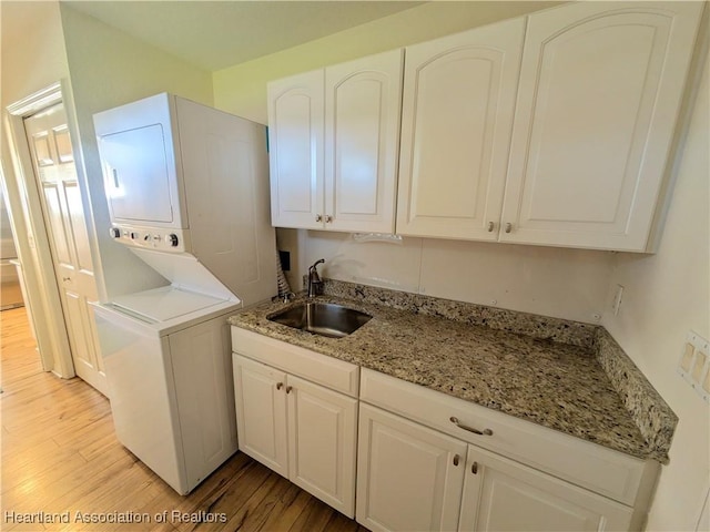 washroom with cabinets, light wood-type flooring, sink, and stacked washer and clothes dryer