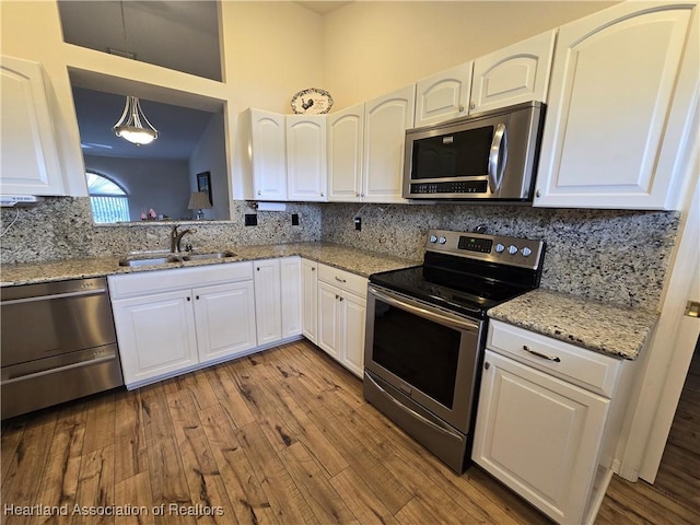 kitchen with white cabinets, sink, light stone countertops, appliances with stainless steel finishes, and decorative light fixtures