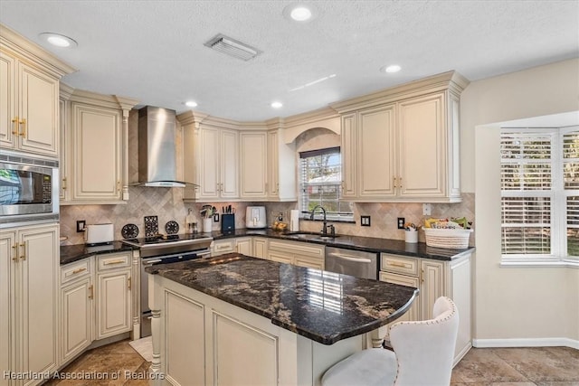 kitchen featuring wall chimney exhaust hood, cream cabinetry, a sink, and appliances with stainless steel finishes