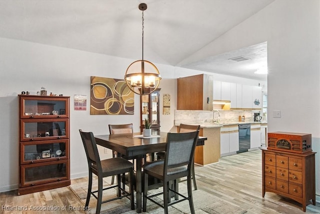 dining space featuring an inviting chandelier, light hardwood / wood-style floors, sink, and vaulted ceiling