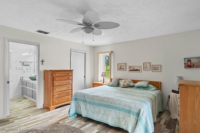 bedroom with ceiling fan, a textured ceiling, connected bathroom, and light hardwood / wood-style flooring