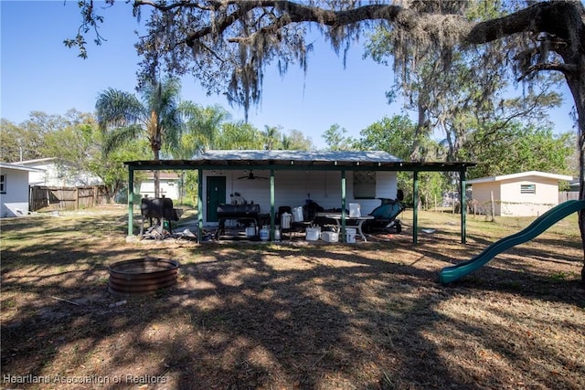 back of property with a ceiling fan, a playground, and fence