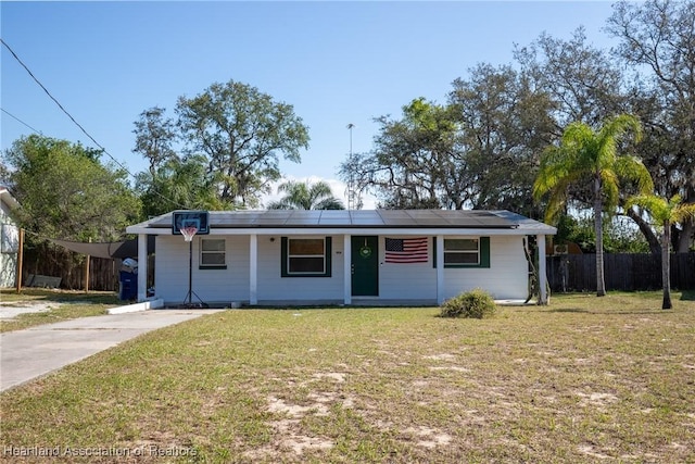 view of front of home featuring concrete driveway, a front lawn, fence, and solar panels