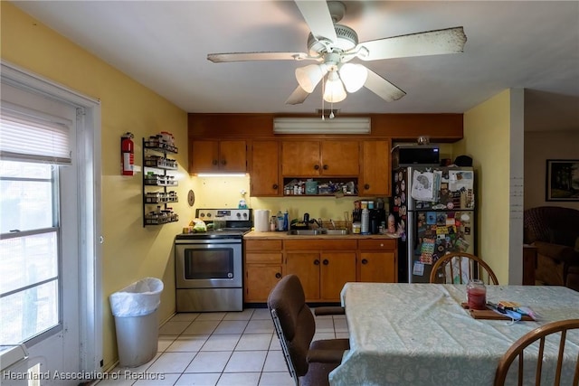 kitchen with a sink, brown cabinetry, light tile patterned flooring, stainless steel electric range oven, and freestanding refrigerator