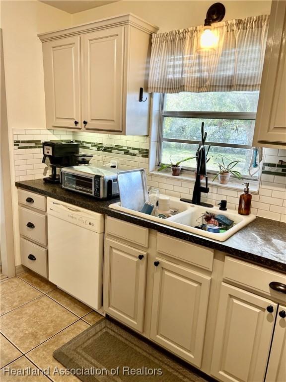 kitchen featuring light tile patterned floors, white dishwasher, sink, white cabinetry, and tasteful backsplash