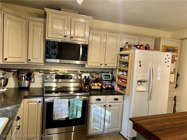 kitchen featuring light tile patterned flooring, dark stone countertops, tasteful backsplash, and appliances with stainless steel finishes