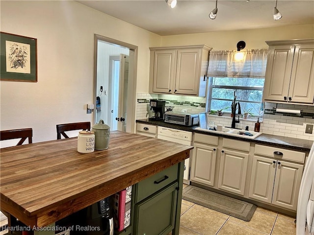 kitchen featuring light tile patterned floors, butcher block countertops, backsplash, white cabinetry, and sink