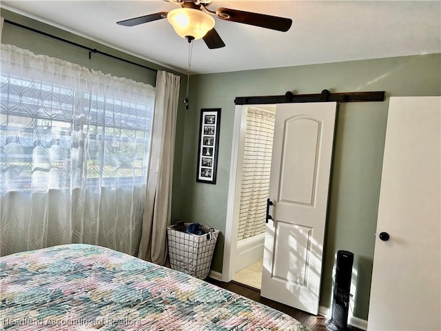 bedroom featuring ceiling fan, a barn door, and dark wood-type flooring