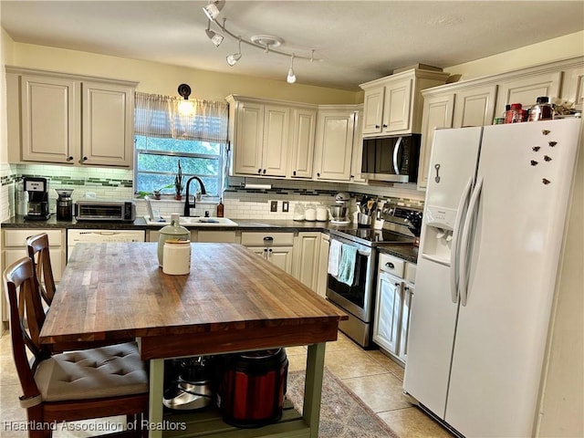 kitchen with light tile patterned floors, butcher block countertops, backsplash, appliances with stainless steel finishes, and sink