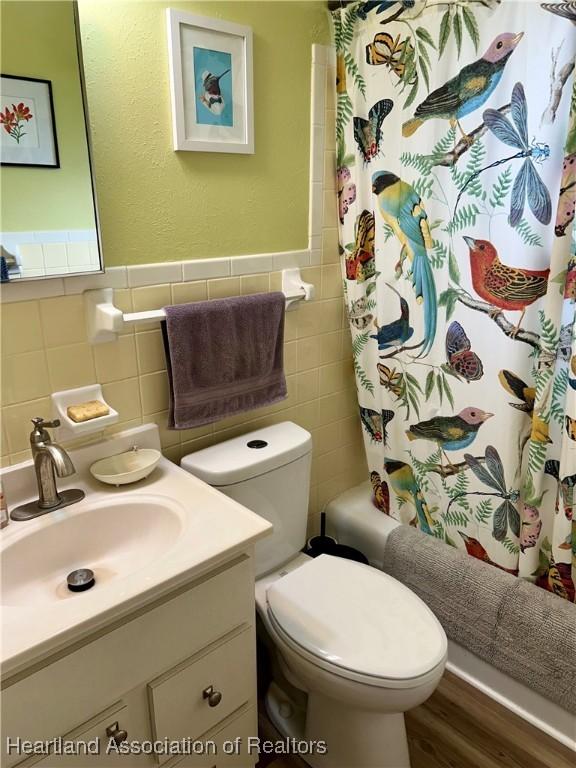 full bathroom featuring toilet, vanity, tile walls, and shower / bath combo with shower curtain