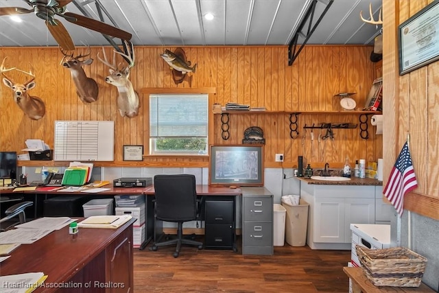 home office with dark wood-type flooring, ceiling fan, sink, and wood walls