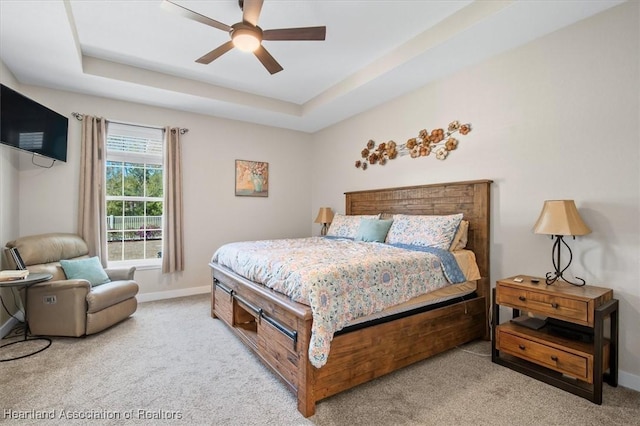 bedroom with a raised ceiling, light colored carpet, and ceiling fan