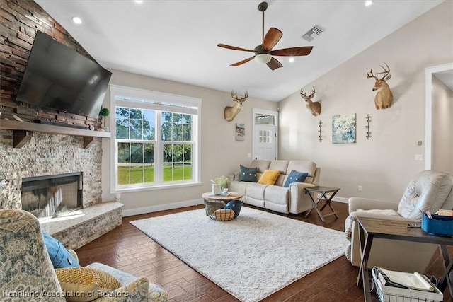 living room featuring vaulted ceiling, a stone fireplace, dark hardwood / wood-style floors, and ceiling fan