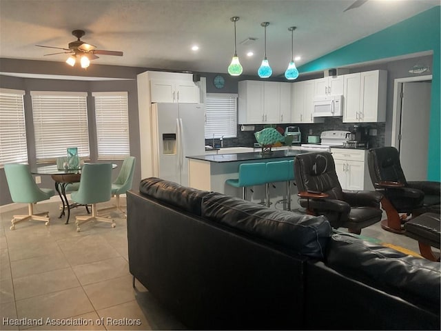 kitchen featuring white cabinetry, tasteful backsplash, pendant lighting, vaulted ceiling, and white appliances