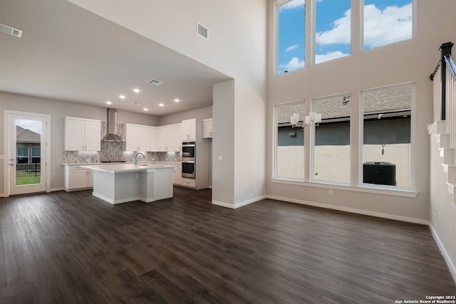 kitchen featuring wall chimney exhaust hood, a healthy amount of sunlight, and an island with sink