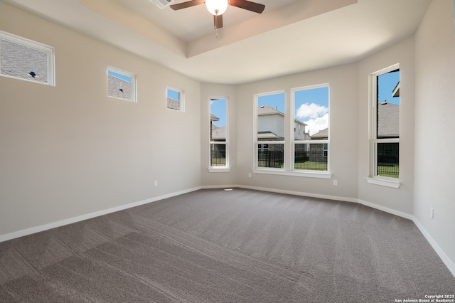 empty room featuring ceiling fan, dark colored carpet, and a raised ceiling