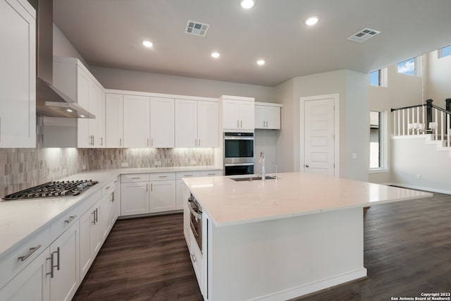 kitchen featuring appliances with stainless steel finishes, tasteful backsplash, wall chimney range hood, dark hardwood / wood-style floors, and white cabinets